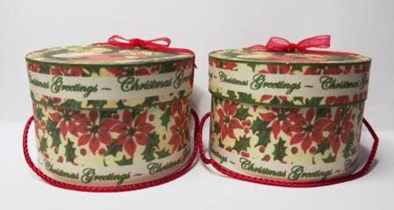 May include: Two round, white gift boxes with red ribbon bows. The boxes are decorated with a green and red floral pattern and the text "Christmas Greetings".