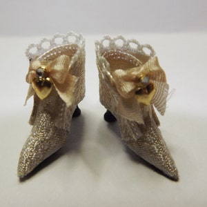 May include: A pair of miniature white satin shoes with gold trim and a heart-shaped embellishment. The shoes have a lace trim around the top and a bow on the front.