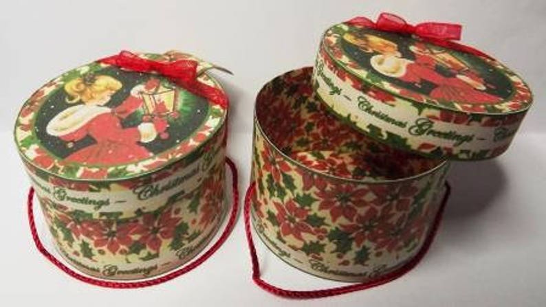 May include: Two round, red and green Christmas gift boxes with a poinsettia design. The boxes have a white ribbon and the text "Christmas Greetings".