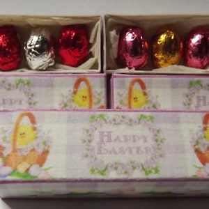 May include: Two small boxes with a pink and white checkered pattern and a floral design. The boxes have the words "Happy Easter" printed on them. Each box contains six chocolate eggs wrapped in foil. The eggs are silver, red, and gold.