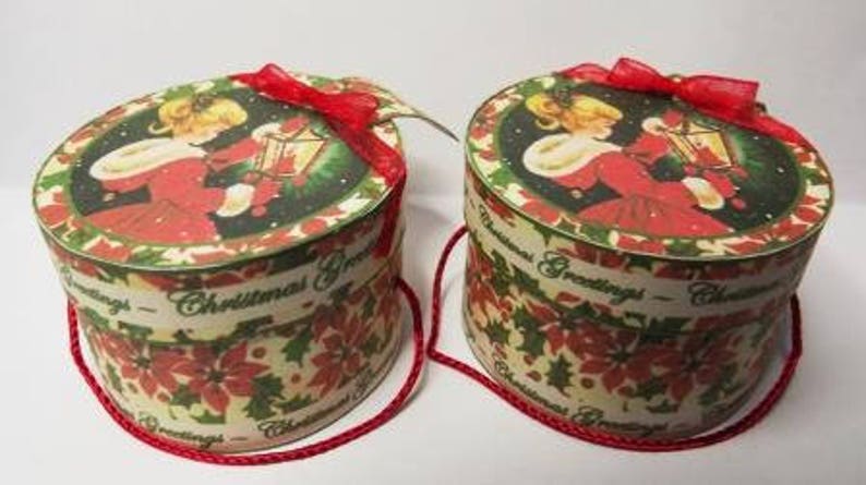 May include: Two round Christmas gift boxes with red ribbon bows and a white background with a green and red floral pattern. The boxes have the text "Christmas Greetings" on them.
