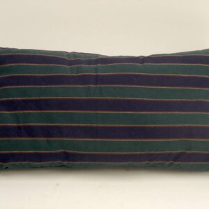 May include: Rectangular pillow with a green background and horizontal stripes in navy blue and burgundy. The pillow is a solid color with a simple design, suitable for a bed or couch.