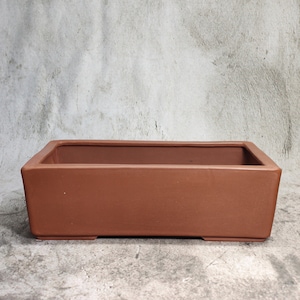 Pode incluir: Um vaso retangular de bonsai de terracota com um acabamento liso e sem esmalte. O vaso tem uma borda ligeiramente elevada e uma base plana.