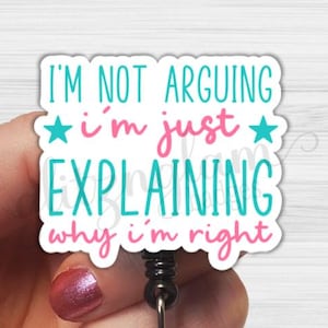 May include: A white badge reel with the text "I'M NOT ARGUING i'm just EXPLAINING why i'm right" in teal and pink. The badge reel has a black retractable cord and a clear plastic holder with a decorative silver-colored gem.
