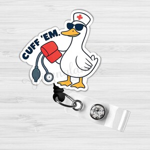 May include: A white badge reel with a cartoon duck wearing sunglasses and a nurse's hat, holding a blood pressure cuff. The text "CUFF 'EM." is above the duck. The reel has a clear plastic strap and a silver-colored metal clip.