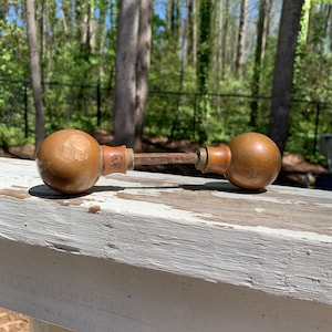 May include: A pair of antique brass door knobs with a worn finish. The knobs are round and have a simple design. They are resting on a white painted wooden surface.