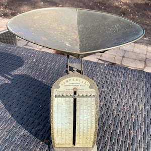 May include: An antique Imperial Computing Confectionery Scale with a large, oval-shaped pan. The scale is made of metal with a weathered appearance, featuring a detailed face with weight measurements in pounds and ounces. The text "Warranted Accurate" is visible.