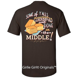 May include: Brown t-shirt with a graphic of cornbread and the text "Some of y'alls cornbread ain't done in the middle!"  Girlie Girl Originals is printed at the bottom.