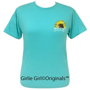 May include: A turquoise blue t-shirt with a yellow sunflower graphic and the text "Girlie Girl Originals" printed on the front.