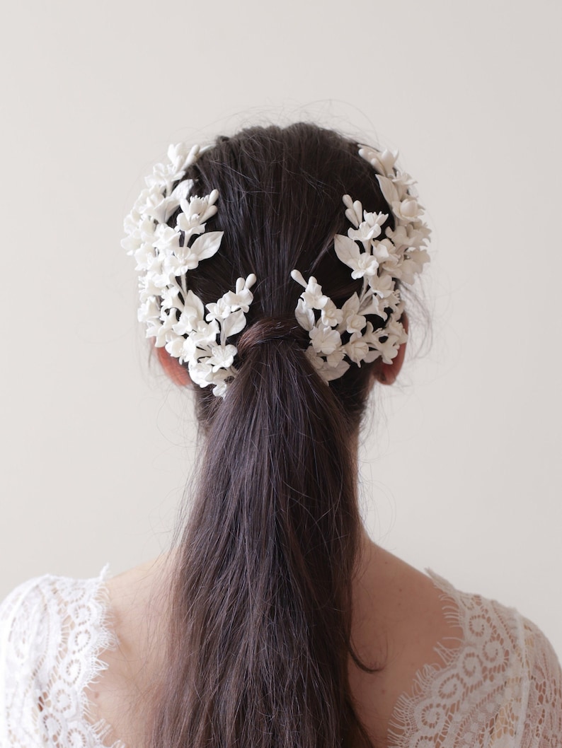 May include: White floral hairpiece with delicate flowers and leaves. The hairpiece is worn in the hair, creating a crown-like effect.