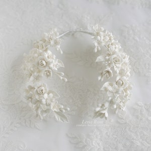 May include: White floral hair comb with delicate white flowers and leaves. The comb is made of porcelain and is perfect for a wedding or special occasion.