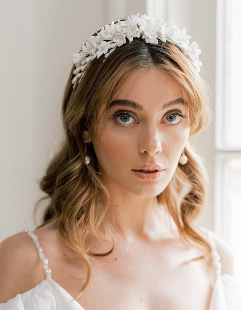 May include: A white floral headband with delicate white flowers. The headband is made of fabric and has a simple design.