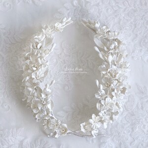 May include: White floral hairpiece made of delicate porcelain flowers. The piece is shaped like a crown and is perfect for a wedding or special occasion.
