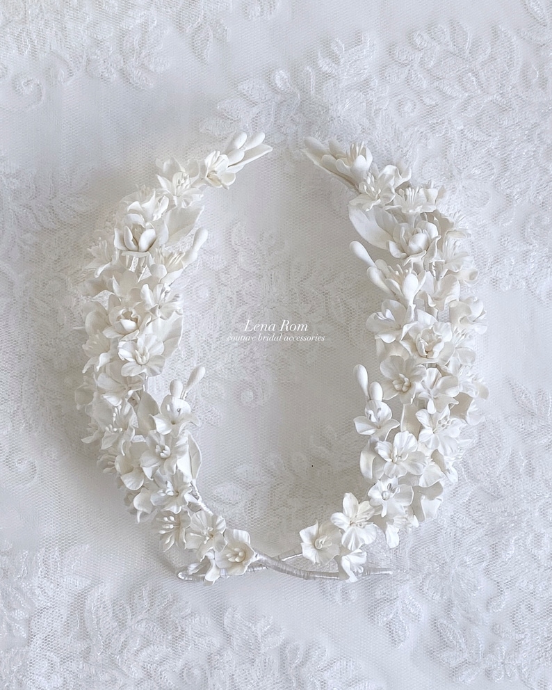 May include: White floral hairpiece made of delicate porcelain flowers. The piece is shaped like a crown and is perfect for a wedding or special occasion.
