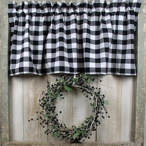 May include: Black and white checkered valance with a gathered ruffle, hanging in a window with a wooden frame. A black berry wreath hangs below the valance.