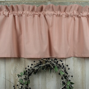 May include: A pink and white striped valance with a ruffled edge. The valance is hanging in a window frame.