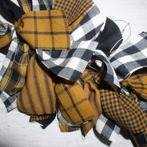 May include: A handmade fabric wreath with a mix of black and white buffalo check, and yellow and black plaid fabric.