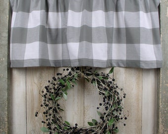 May include: A gray and white checkered valance hangs above a decorative wreath. The wreath is made of twigs, green leaves, and black berries. The valance is made of a soft fabric and is gathered at the top.