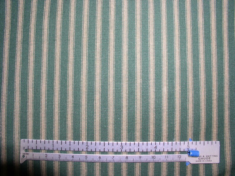 May include: A close-up of a green and white striped fabric with a ruler measuring 5 inches. The fabric has a subtle texture and a classic striped pattern.