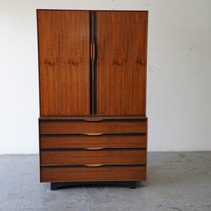 May include: A mid-century modern armoire with a wood veneer finish and four drawers. The armoire has a dark wood frame and black hardware.