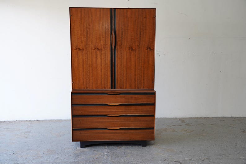 May include: A mid-century modern armoire with a wood veneer finish and four drawers. The armoire has a dark wood frame and black hardware.