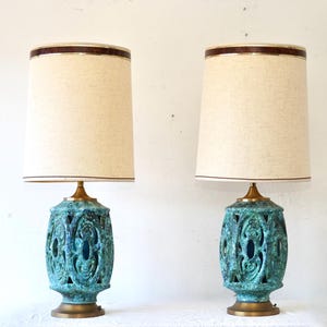 May include: Pair of vintage table lamps. Each lamp features a teal ceramic base with an openwork design, a beige fabric shade, and brass accents. The lamps are approximately 28 inches tall.