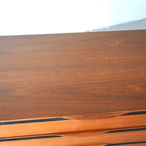 May include: A wooden dresser with six drawers. The top drawer is closed and the rest are open. The dresser has black trim around the drawers.