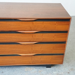 May include: A wooden dresser with six drawers and black trim. The drawers have curved wooden handles.