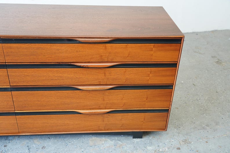 May include: A wooden dresser with six drawers and black trim. The drawers have curved wooden handles.
