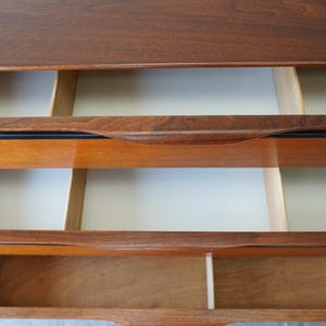 May include: A wooden dresser with three drawers. The top drawer is closed, and the bottom two drawers are open, revealing the empty interior.