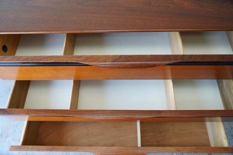 May include: A wooden dresser with three drawers. The top drawer is closed, and the bottom two drawers are open, revealing the empty interior.
