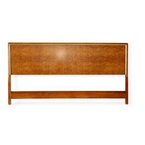 May include: A rectangular wooden headboard featuring a central panel with a vertical ribbed texture and a burl wood grain pattern. The headboard is framed by a thin gold-colored metal trim and supported by two vertical legs connected by a horizontal base rail.