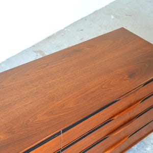 May include: A wooden dresser with six drawers and black trim. The drawers have curved wooden handles.
