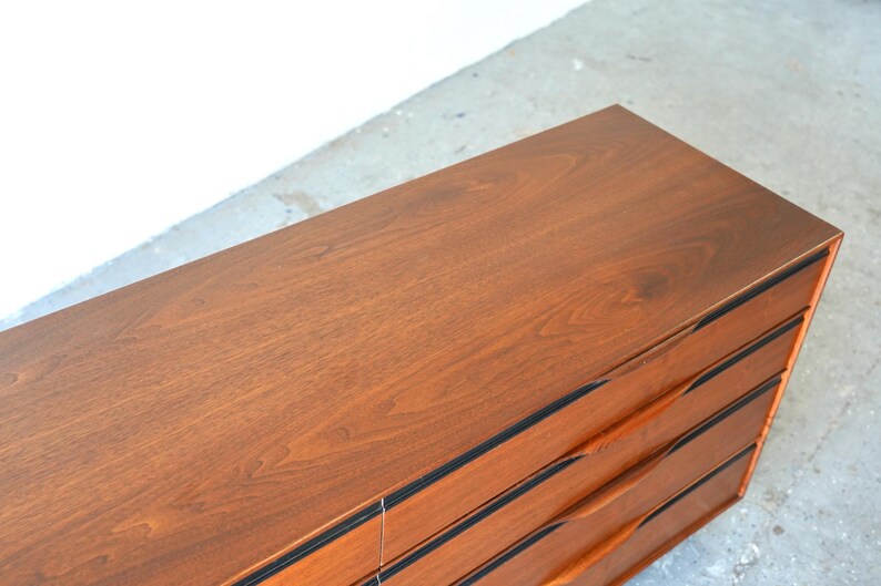May include: A wooden dresser with six drawers and black trim. The drawers have curved wooden handles.