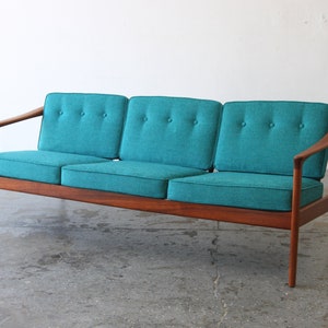 May include: A teal three-seater sofa with a wooden frame and curved arms. The sofa has button tufting on the cushions.