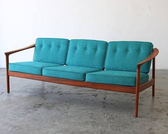 May include: A teal three-seater sofa with a wooden frame and curved arms. The sofa has button tufting on the cushions.