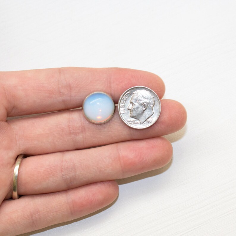 Peut inclure: Un seul clou d'oreille opalescent avec une lunette en argent, &agrave; c&ocirc;t&eacute; d'une pi&egrave;ce de 10 cents am&eacute;ricaine pour la comparaison de taille. La boucle d'oreille a un aspect doux et brillant, avec une couleur bleu clair et blanche. La pi&egrave;ce montre le profil de Franklin D. Roosevelt.
