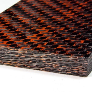 Puede incluir: Primer plano de una lámina de fibra de carbono negra y naranja. La lámina tiene una textura tejida en capas. La lámina es un material utilizado en la elaboración artesanal.