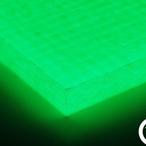 Puede incluir: Primer plano de una lámina de fibra de carbono verde con un borde en capas. La lámina tiene una superficie texturizada y brilla bajo una luz negra.