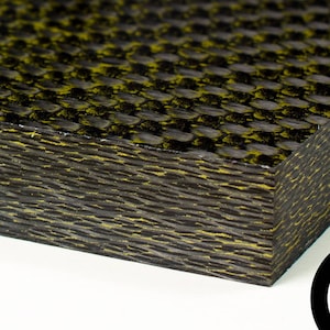 Puede incluir: Primer plano de una lámina de fibra de carbono negra y amarilla. La lámina tiene un patrón tejido y está en capas. La lámina es un material utilizado en la fabricación.