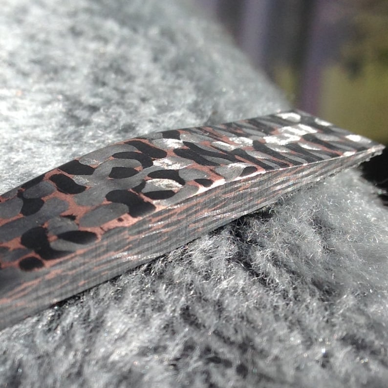 May include: Close-up of a black and silver patterned metal bar with a slightly curved shape. The bar has a layered, laminated appearance.