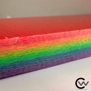 Puede incluir: Un bloque rectangular con una superficie superior roja lisa y brillante, y un perfil lateral que muestra una transición degradada multicolor en capas desde el rojo al naranja, amarillo, verde, azul y violeta. El logo Carbonwaves es visible.