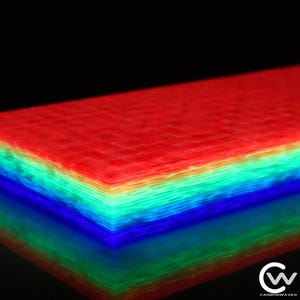 May include: A multi-layered material with a gradient of colours from red to blue. The layers are illuminated, creating a vibrant, glowing effect. The bottom of the stack reflects the colours. The Carbonwaves logo is in the bottom right corner.
