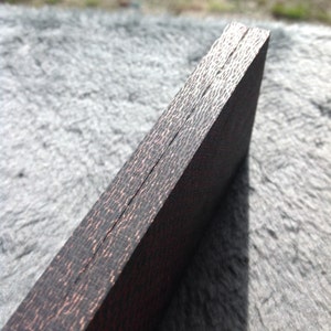 May include: Close-up of the edge of a dark wood box with a copper-coloured finish. The box is made of two pieces of wood that are joined together with a thin seam.