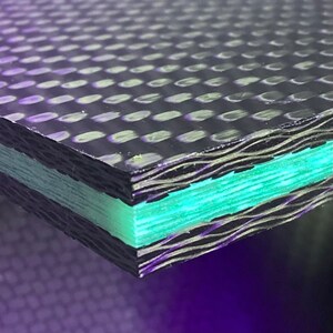 Puede incluir: Primer plano de una lámina de fibra de carbono negra con una capa verde debajo. La lámina tiene una superficie texturizada con un patrón de pequeños círculos.
