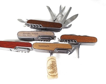 May include: Four multi-tool pocket knives with wooden handles. The handles are engraved with different sayings: "Fortune favors the bold", "Lionheart", and two others. A cork with a grape design is in the center.