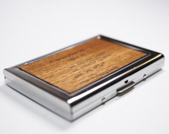 May include: A silver metal card holder with a wooden insert. The wood has a quote engraved on it: "Everything in life we choose to love, we choose to live, and the life we live, is a reflection of our choices."