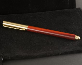 May include: A wooden pen with a gold-colored metal trim. The pen is lying on a black velvet surface.