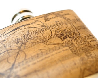 May include: A brown leather flask with a silver cap and a laser-etched design of a skeleton playing music on a sheet of music.