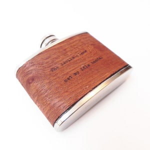 May include: A silver and wood flask with the text "The devilish lang wet by little hands" engraved on the wood.